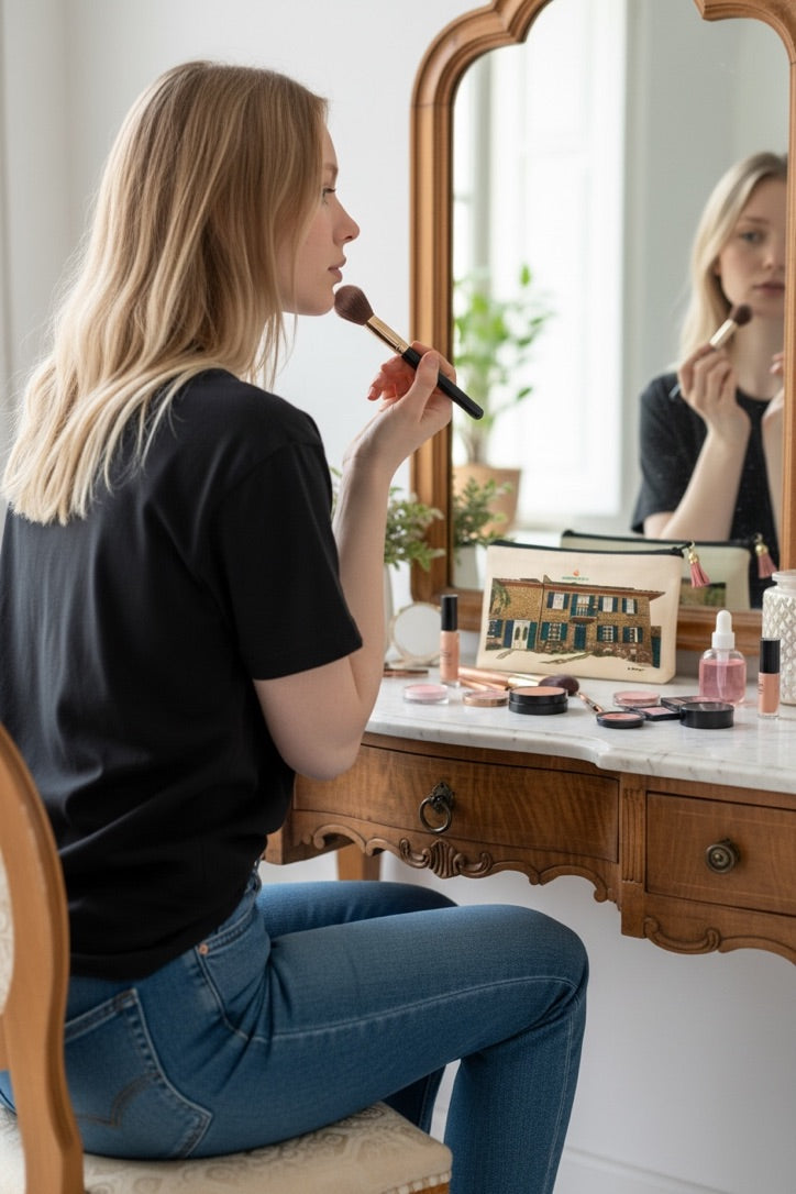 alt="Femme utilisant la pochette maquillage beige sublimée Oshiny Art & Lifestyle motif Barbera & Tulipani, accessoire de voyage personnalisé maison d'hôtes"